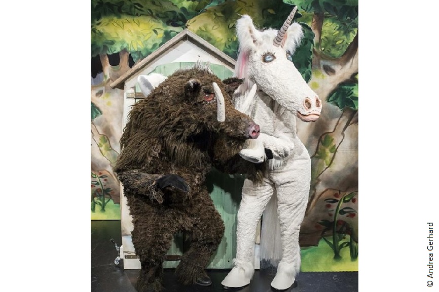 Das Bild von zwei Personen in einem Einhornkostüm und einem Wildschweinkostüm auf einer Bühne.